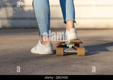Vue rognée d'un patineur méconnaissable qui monte sur son plateau de skate au parc municipal avec une sneaker et un Jean qui se faufile contre un mur blanc Banque D'Images