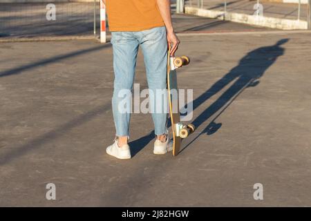 Vue courte d'un jeune homme tenant une longue planche sur ses mains portant une tenue de rue différente avec lumière de l'après-midi au coucher du soleil Banque D'Images