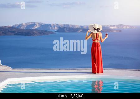 Une femme dans une élégante robe rouge se tient près de la piscine et bénéficie de la vue sur la mer Égée Banque D'Images