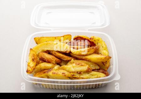 Quartiers de pommes de terre cuits dans une boîte en plastique transparente de qualité alimentaire pour la réfrigération ou le stockage, sur fond gris clair Banque D'Images