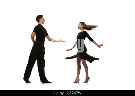 Portrait dynamique de jeunes danseurs émotifs vêtus de tenues noires dansant danse de salle de bal isolée sur fond blanc. Concept d'art, beauté, musique, style. Banque D'Images