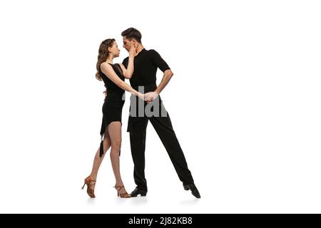 Portrait dynamique de jeunes danseurs émotifs vêtus de tenues noires dansant danse de salle de bal isolée sur fond blanc. Concept d'art, beauté, musique, style. Banque D'Images