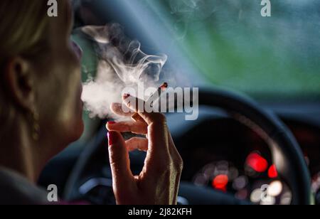11 mai 2022, Schleswig-Holstein, Flensburg: Une femme est assise derrière le volant de sa voiture avec une cigarette allumée. Photo: Axel Heimken/dpa Banque D'Images