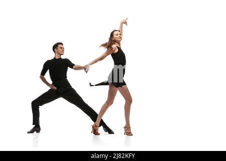 Portrait dynamique de jeunes danseurs émotifs vêtus de tenues noires dansant danse de salle de bal isolée sur fond blanc. Concept d'art, beauté, musique, style. Banque D'Images