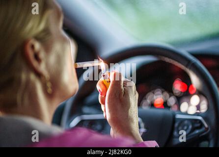11 mai 2022, Schleswig-Holstein, Flensburg: Une femme allume une cigarette derrière le volant de sa voiture. Photo: Axel Heimken/dpa Banque D'Images