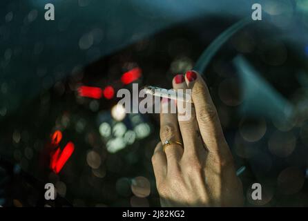 11 mai 2022, Schleswig-Holstein, Flensburg: Une femme est assise derrière le volant de sa voiture avec une cigarette allumée. Photo: Axel Heimken/dpa Banque D'Images
