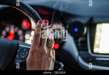 11 mai 2022, Schleswig-Holstein, Flensburg: Une femme est assise derrière le volant de sa voiture avec une cigarette allumée. Photo: Axel Heimken/dpa Banque D'Images