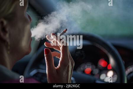 11 mai 2022, Schleswig-Holstein, Flensburg: Une femme est assise derrière le volant de sa voiture avec une cigarette allumée. Photo: Axel Heimken/dpa Banque D'Images