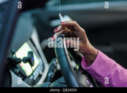 11 mai 2022, Schleswig-Holstein, Flensburg: Une femme est assise derrière le volant de sa voiture avec une cigarette allumée. Photo: Axel Heimken/dpa Banque D'Images