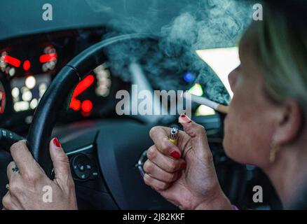 11 mai 2022, Schleswig-Holstein, Flensburg: Une femme allume une cigarette derrière le volant de sa voiture. Photo: Axel Heimken/dpa Banque D'Images