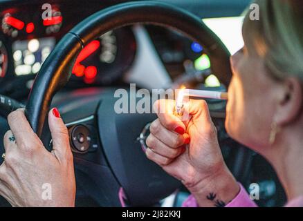 11 mai 2022, Schleswig-Holstein, Flensburg: Une femme allume une cigarette derrière le volant de sa voiture. Photo: Axel Heimken/dpa Banque D'Images