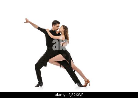 Portrait dynamique de jeunes danseurs émotifs vêtus de tenues noires dansant danse de salle de bal isolée sur fond blanc. Concept d'art, beauté, musique, style. Banque D'Images