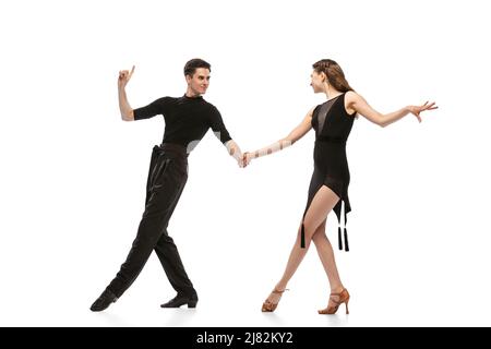 Portrait dynamique de jeunes danseurs émotifs vêtus de tenues noires dansant danse de salle de bal isolée sur fond blanc. Concept d'art, beauté, musique, style. Banque D'Images