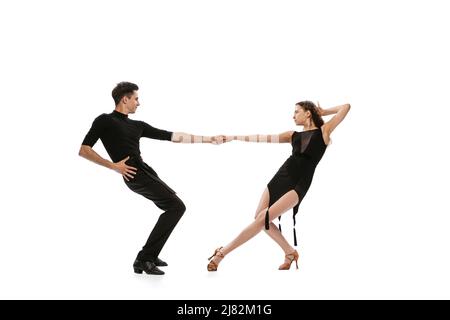 Portrait dynamique de jeunes danseurs émotifs vêtus de tenues noires dansant danse de salle de bal isolée sur fond blanc. Concept d'art, beauté, musique, style. Banque D'Images