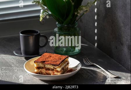 Dessert italien traditionnel tiramisu, café et bouquet de lys de la vallée sur fond de béton gris. Banque D'Images