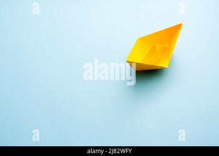 Bateau en papier jaune sur fond bleu avec espace de copie libre pour le texte. Banque D'Images