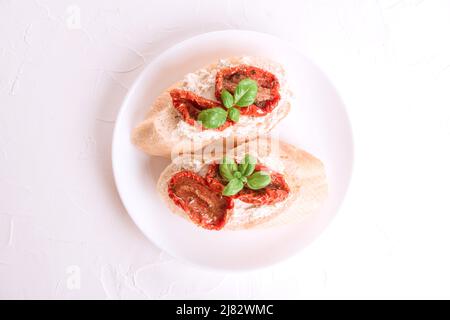 Vue de dessus sur les bruschettas ou toasts avec le fromage ricotta et les tomates séchées au soleil surmontées de basilic sur une assiette blanche, fond de table blanc. Une délicieuse classe Banque D'Images