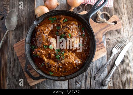Cuisses de poulet à la sauce aux oignons bruns dans une poêle rustique en fonte sur fond de table en bois. Vue de dessus avec espace de copie Banque D'Images