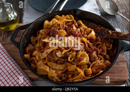 Viande de poulet braisée à la tomate, sauce aux herbes et pâtes dans une casserole rustique en fonte. Cuisine italienne. Banque D'Images