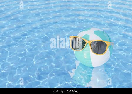 3D réalisation de lunettes de soleil jaunes tendance sur ballon de plage gonflable rayé flottant dans l'eau ondulée de la piscine extérieure le jour d'été Banque D'Images