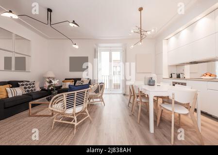 Séjour avec cuisine ouverte avec mobilier blanc, table à manger avec chaises en bois assorties, fauteuils en osier et canapés capitonnés de tissu bleu Banque D'Images