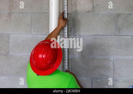 un ouvrier de la construction mesure la hauteur du mur pour couper les goujons de charpente en acier galvanisé. Banque D'Images