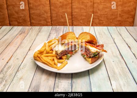 Délicieux hamburger de bœuf cuisiné à l'américaine avec des œufs frits, du bacon, de la laitue, du pain de brioche et une portion de frites Banque D'Images