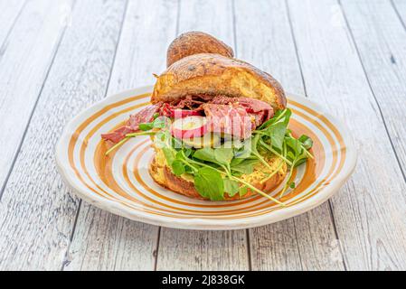 Sandwich avec muffin à la brioche, tranches de pastrami, pousses de laitue, concombre mariné, tranches de radis et huile d'olive Banque D'Images