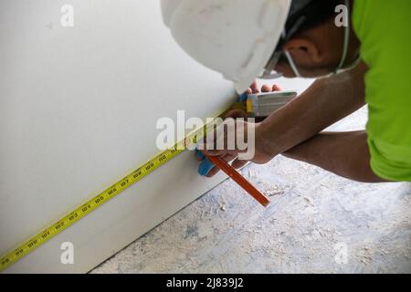 Ouvrier de construction de cloisons sèches mesurant et marquant la cloison sèche pour la couper en forme pour l'installation. Banque D'Images