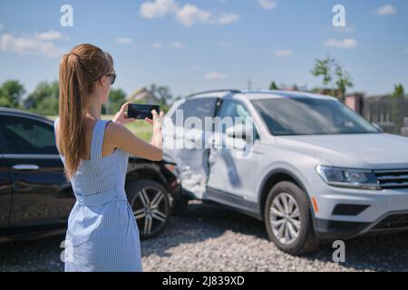 Triste femme pilote photographiant sur le téléphone appareil photo véhicule détruit sur le côté de la rue pour le service d'assurance après accident de voiture.Concept de sécurité routière. Banque D'Images