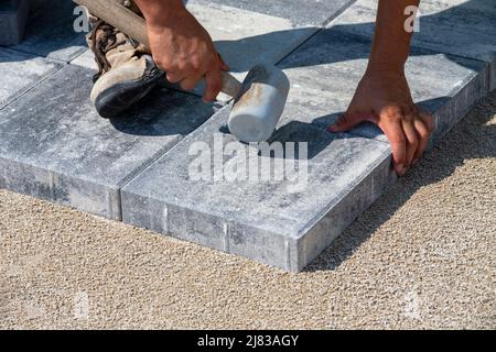 La pierre de pavage est placée et réglée à l'aide d'un marteau en caoutchouc sur une surface de sable préparée Banque D'Images