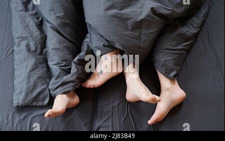 Photo de haut en bas d'un couple de pieds romantiques modernes et méconnaissables découvert dans le lit le matin, linge de lit gris Banque D'Images
