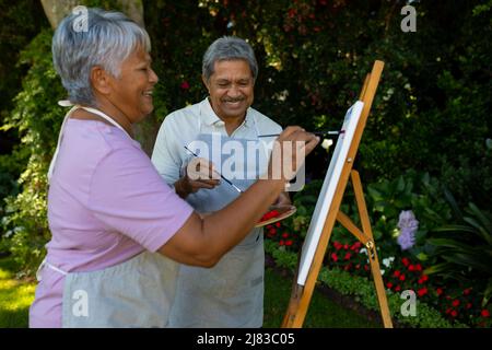 Joyeux couple biracial senior peinture avec aquarelles sur toile contre les plantes dans la cour Banque D'Images