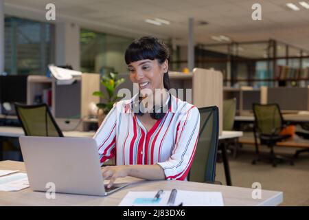 Jeune souriant belle femme biracial conseiller en utilisant un ordinateur portable au bureau dans un lieu de travail moderne Banque D'Images