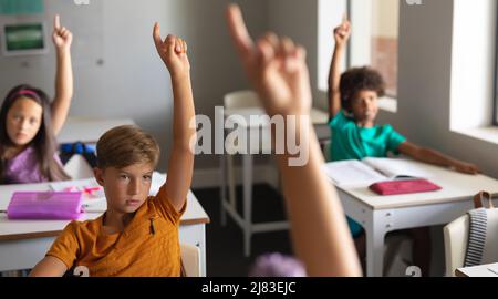 Les élèves multiraciaux de l'école primaire élèvent la main pendant la classe en classe Banque D'Images