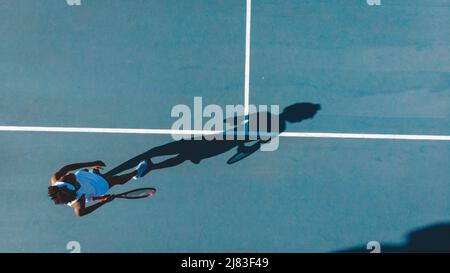 Vue en hauteur d'une jeune joueuse de tennis afro-américaine avec des jeux d'ombre sur un terrain bleu Banque D'Images