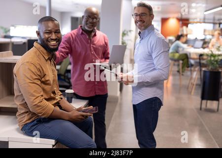 Portrait de collègues hommes d'affaires multiraciaux souriants avec des technologies sans fil dans un bureau moderne Banque D'Images