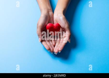 Mains rognées d'une femme afro-américaine de taille moyenne adulte tenant le coeur rouge sur fond bleu Banque D'Images