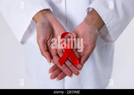 Section médiane des mains du médecin afro-américain moyen adulte avec ruban de sensibilisation Red AIDS Banque D'Images