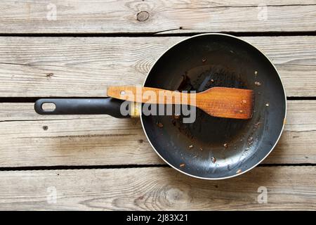 Une poêle et une spatule en bois avec les restes de nourriture frite sur une table en bois à la maison dans la cuisine, vaisselle sale, une vieille poêle Banque D'Images