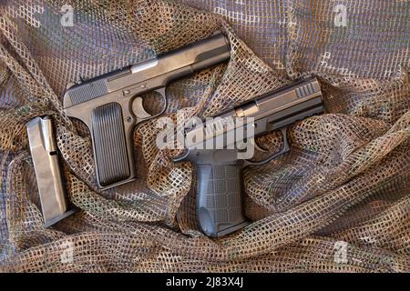 Deux pistolets de combat se trouvent sur un filet protecteur de camouflage, arme militaire, pistolet Banque D'Images