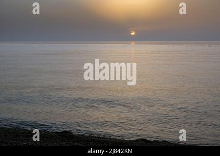 Disque orange du soleil près de la plage avec un mélange de sable et de petits cailloux au coucher du soleil sur la mer Méditerranée Banque D'Images