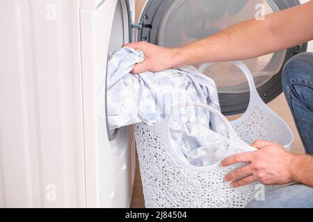 Un homme prend le linge de lit séché hors du sèche-linge. Sèche-linge dans la maison. Banque D'Images