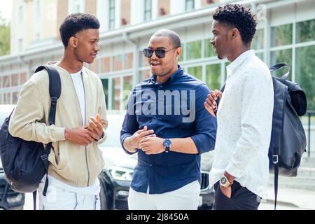 Un groupe de trois étudiants afro-américains branchés et bien habillés qui communiquent dans la rue Banque D'Images