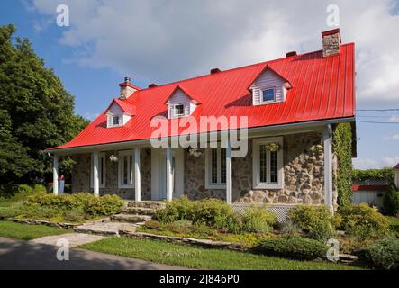 Réplique de l'ancienne maison en pierre de campagne de style cottage Canadiana 1850s avec toit en tôle rouge en été. Banque D'Images