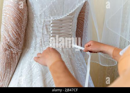 La mariée aide à s'habiller dans une robe de mariage. Laçage. Banque D'Images