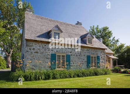 Ancienne maison en pierre de campagne de style cottage Canadiana de 1722 avec garniture bleue et toit en bardeaux en bois de cèdre en été. Banque D'Images