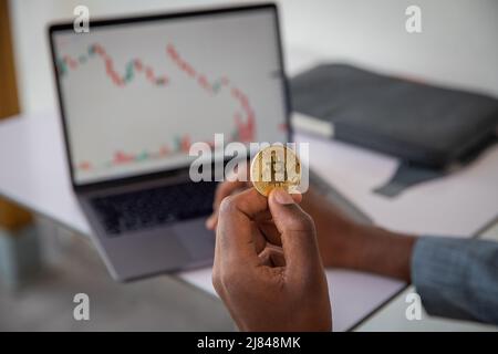 Gros plan d'une pièce de bitcoin tenue dans la main par un investisseur, krach du marché et tableau négatif en rouge, crise financière et concept d'inflation Banque D'Images