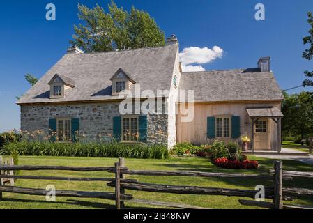 Ancienne maison en pierre de campagne de style cottage Canadiana de 1722 avec garniture bleue et toit en bardeaux en bois de cèdre en été. Banque D'Images