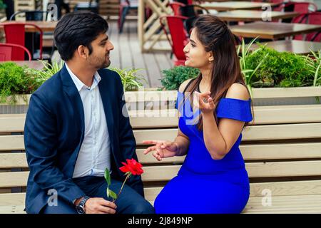 femme indienne brunette aux cheveux longs en robe bleue avec son beau petit ami ayant daté s'ennuyer .homme donnant rose à sa petite amie mal Banque D'Images